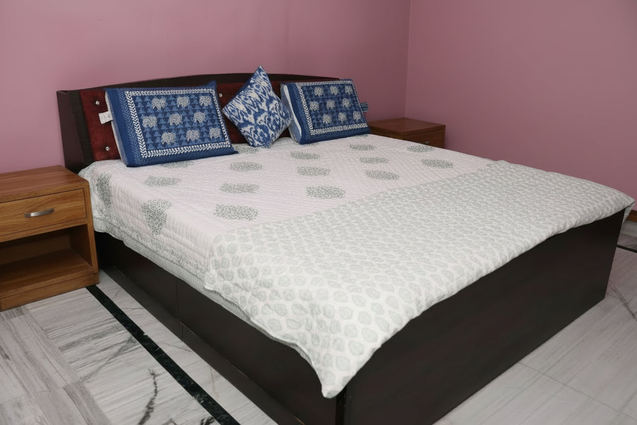 Bedroom with a bed featuring a white quilt and blue pillows, against a pink wall.